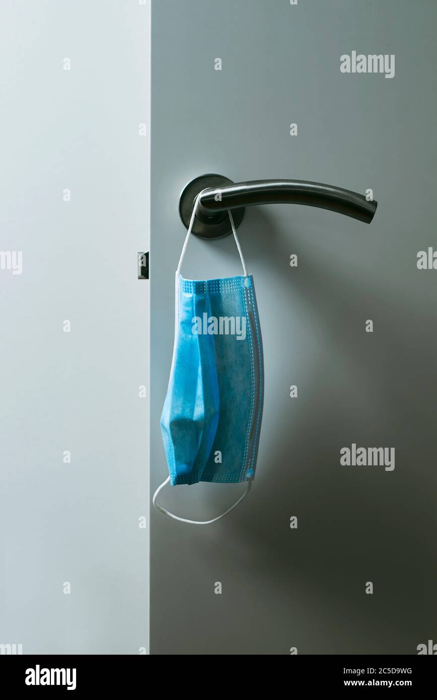 chiusura di una maschera chirurgica blu appesa al moderno pomello di una porta bianca aperta Foto Stock