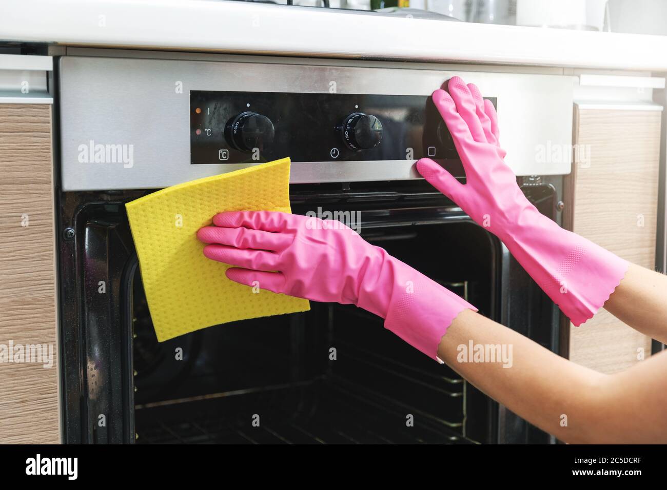 donna mani in guanti protettivi forno di pulizia con straccio giallo in cucina Foto Stock