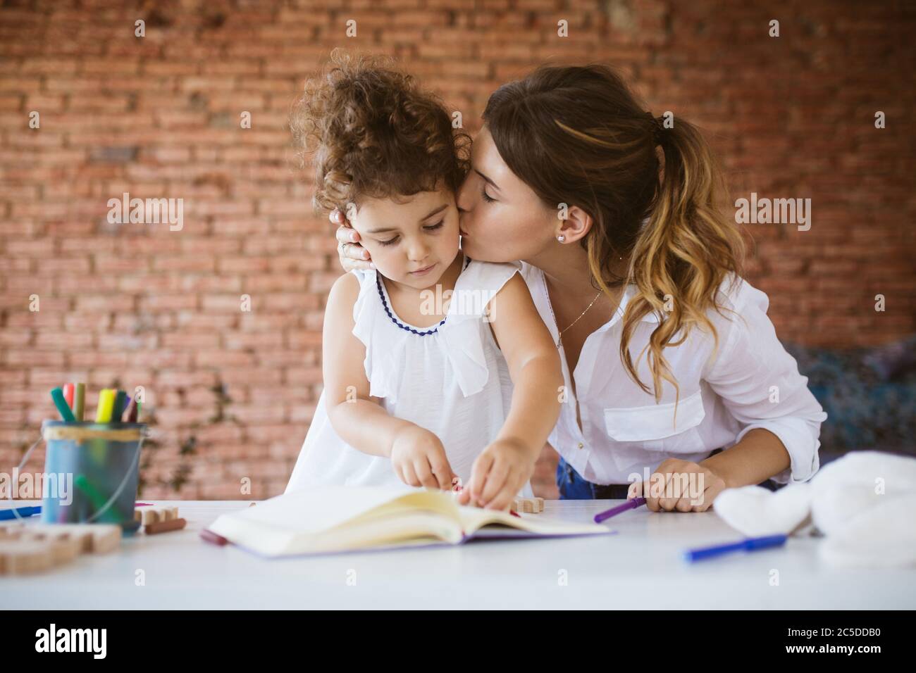 Bella madre in camicia bianca baciare sognatamente la figlia t del bambino Foto Stock