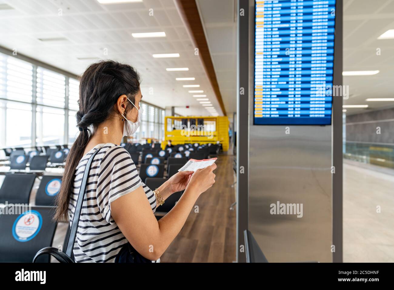 Giovane donna in protezione antivirus maschera di protezione guardando il bordo di informazioni in aeroporto. Interruzione del virus corona. Foto di alta qualità Foto Stock