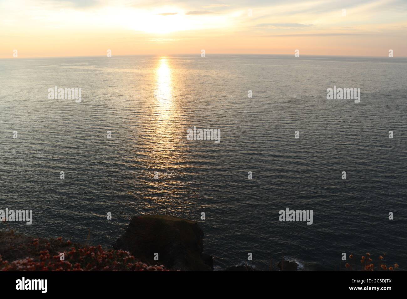 tramonto sull'acqua e scogliera con cielo nuvoloso Foto Stock