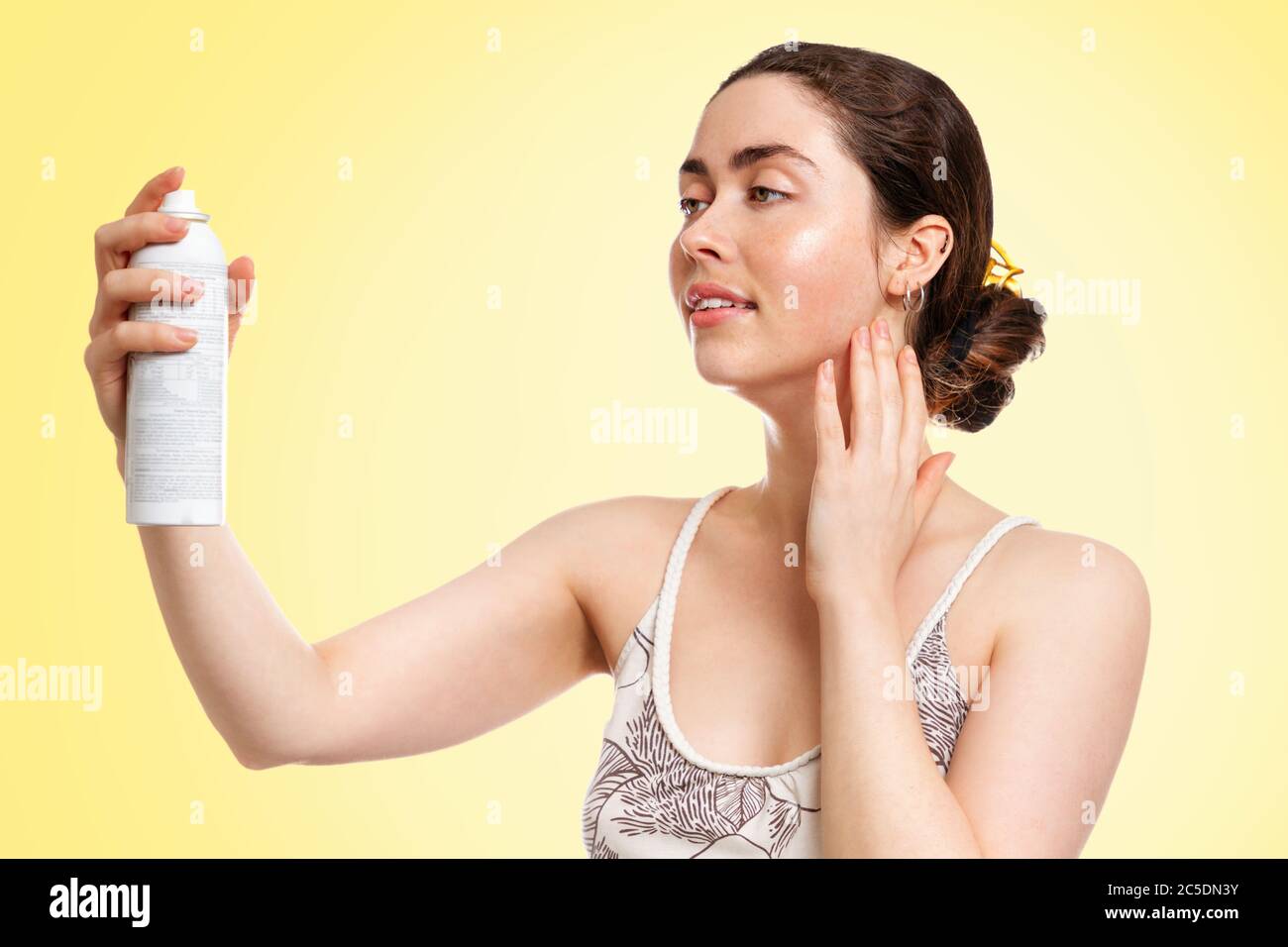 Giovane caucasica con pelle bagnata, con una bottiglia di acqua termale. Sfondo giallo. Il concetto di cosmetologia, cura della pelle e idratazione. Foto Stock