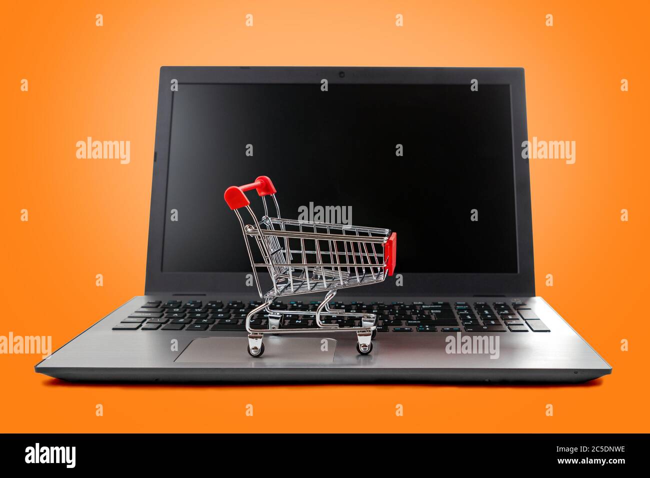 Un computer portatile con un carrello giocattolo sulla tastiera. Isolare su sfondo arancione. Concetto di shopping online e tecnologie moderne. Foto Stock