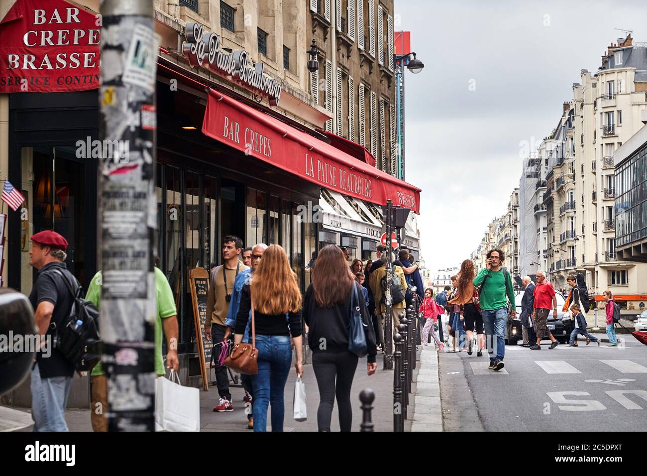 Parigi, Francia - 18 giugno 2015: Un uomo dai capelli ricci in un pullover verde cammina per la strada parlando al telefono. Persone che camminano lungo il marciapiede Foto Stock