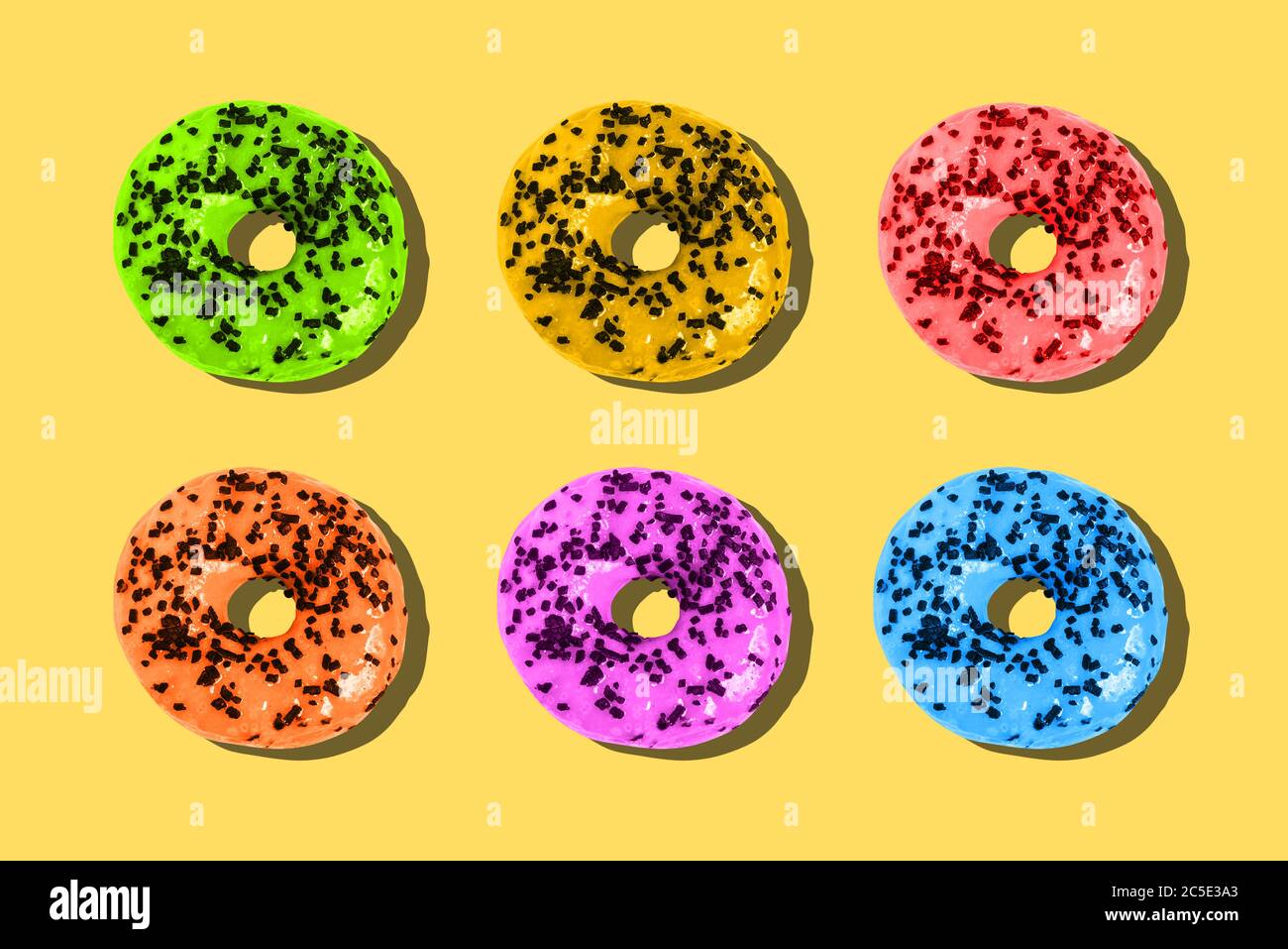 Ciambelle colorate su sfondo giallo. Concetto di estate minimo. Layout piatto, vista dall'alto. Foto Stock
