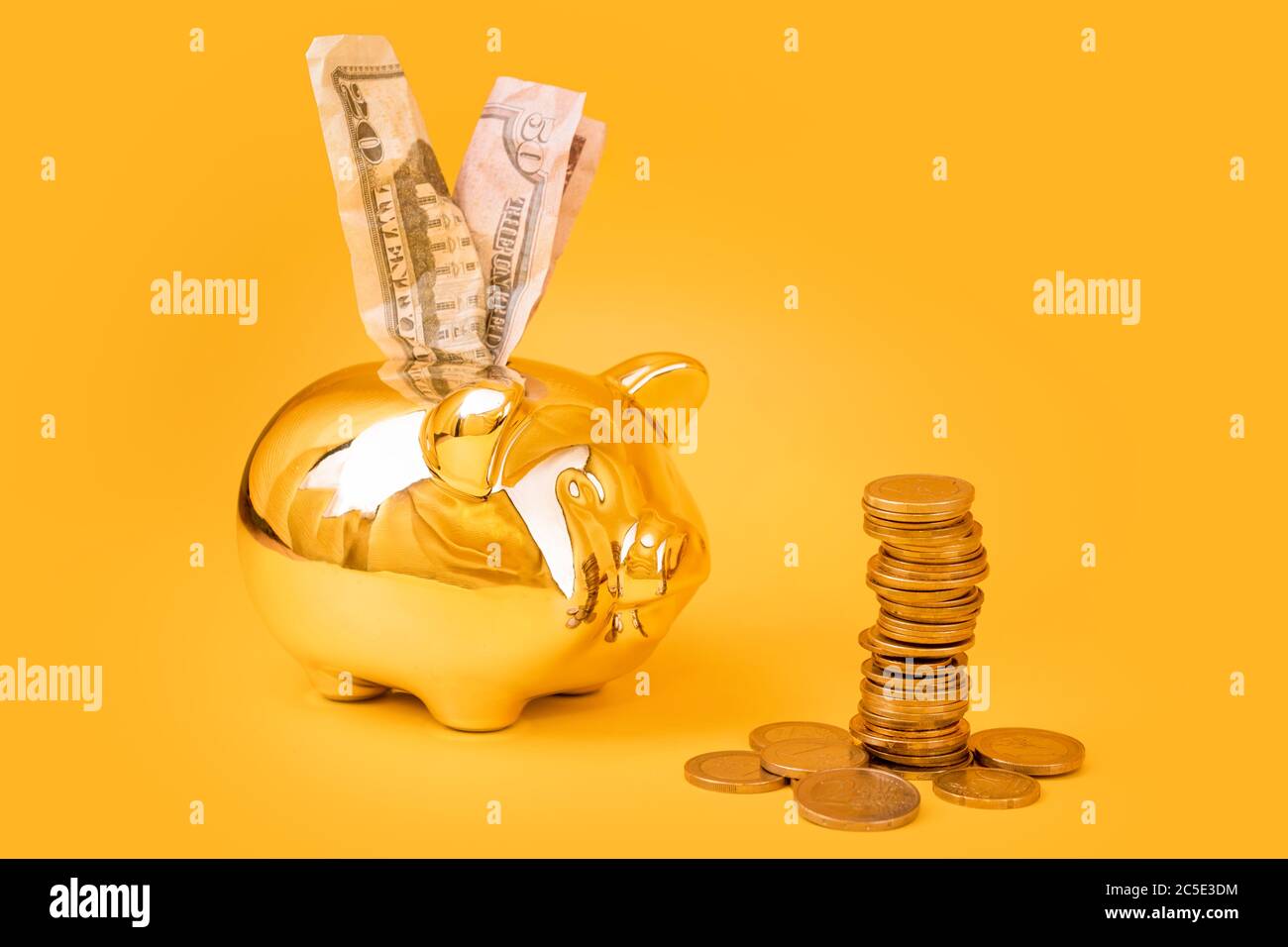 Golden piggy banca con torre di denaro e dollari bollette su sfondo giallo. Pila di monete in euro vicino al contenitore di denaro dorato. Denaro maiale, risparmio di denaro, Moneybox Foto Stock