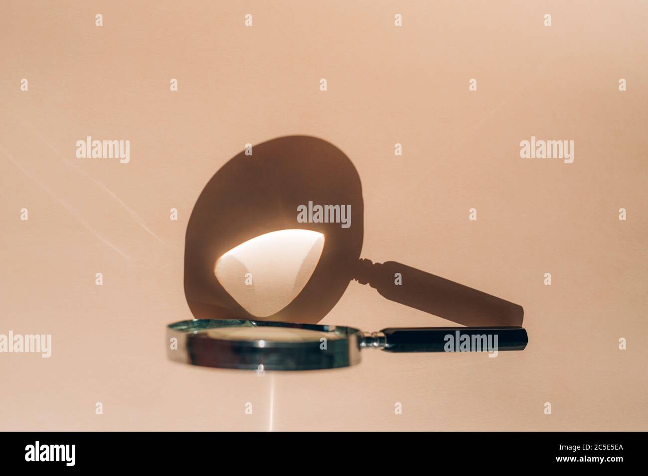 Lente di ingrandimento su sfondo beige con riflesso del sole. Foto Stock