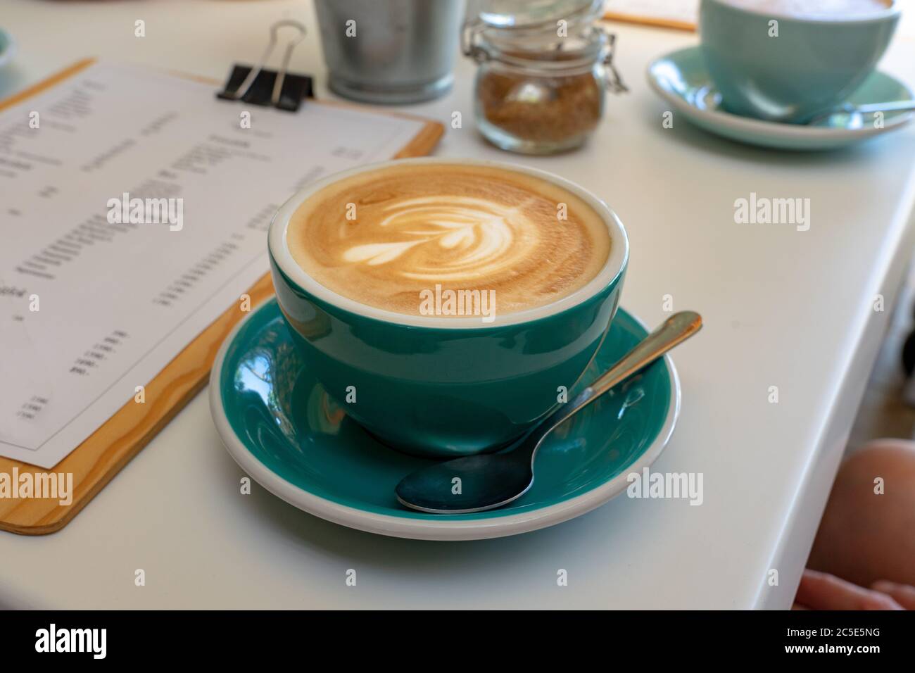 cappuccino caffè latte macchiato in tazza turchese blu in caffetteria con schiuma di latte art . Foto Stock