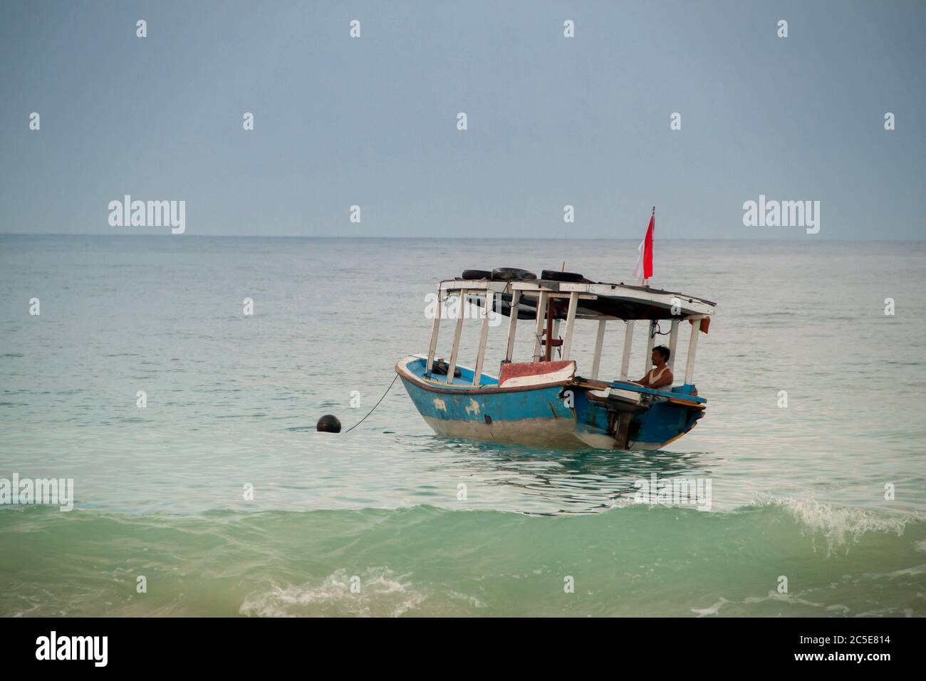 Una barca nel mare di Bali con un uomo seduto all'interno e bandiera indonesiana che sventola Foto Stock