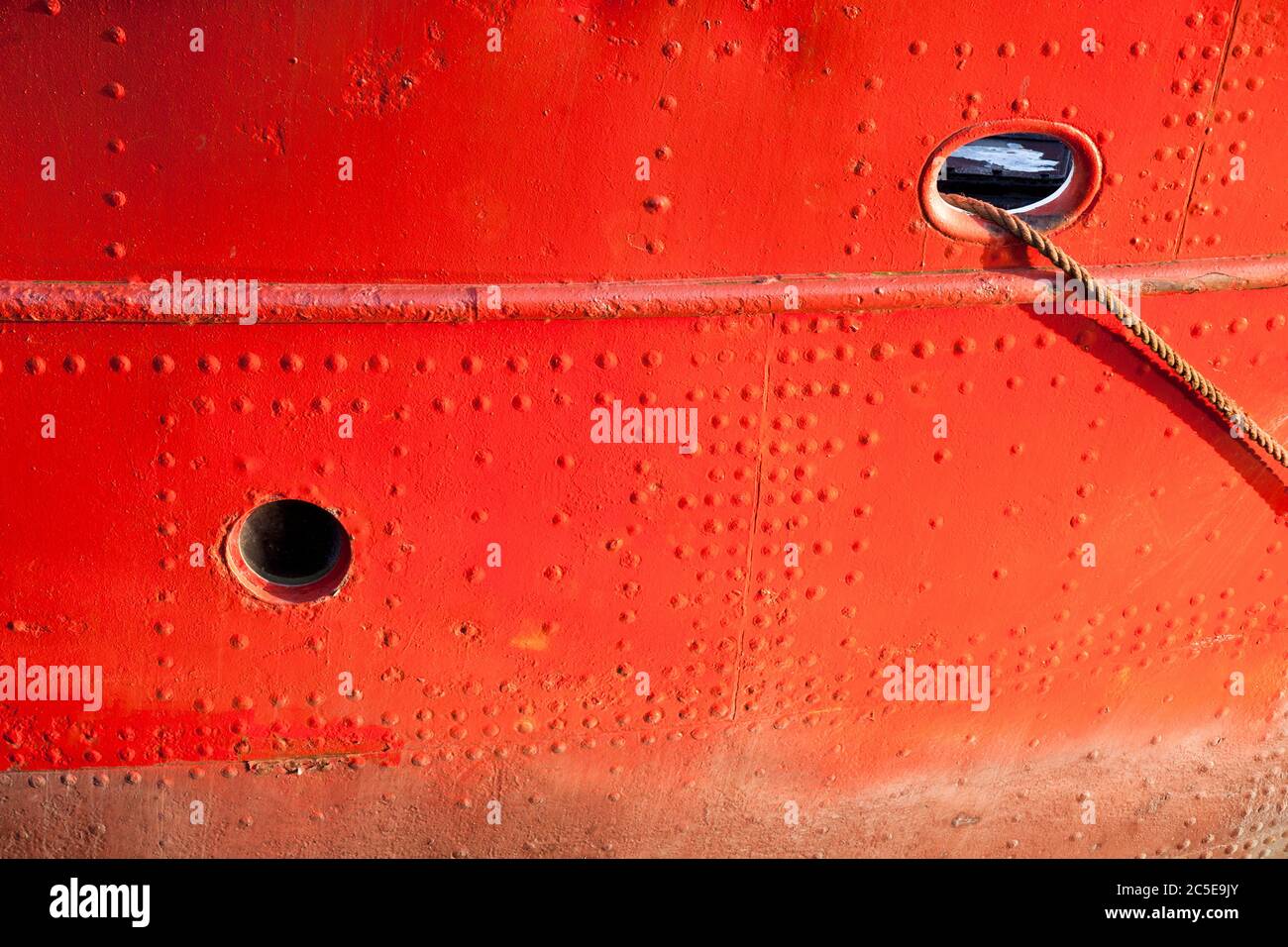 Primo piano dello scafo di una nave dipinta di rosso con un buco portuale e un buco di falda Foto Stock