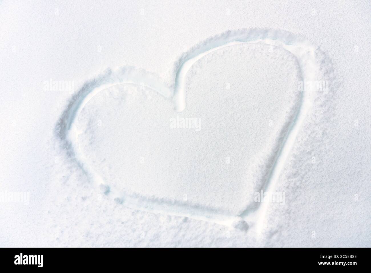 Cuore disegnato su neve fresca texture. Simbolo del cuore sulla superficie nevosa. Concetto di amore, romanticismo e vacanza invernale. Forma del cuore su bianco puro ba Foto Stock