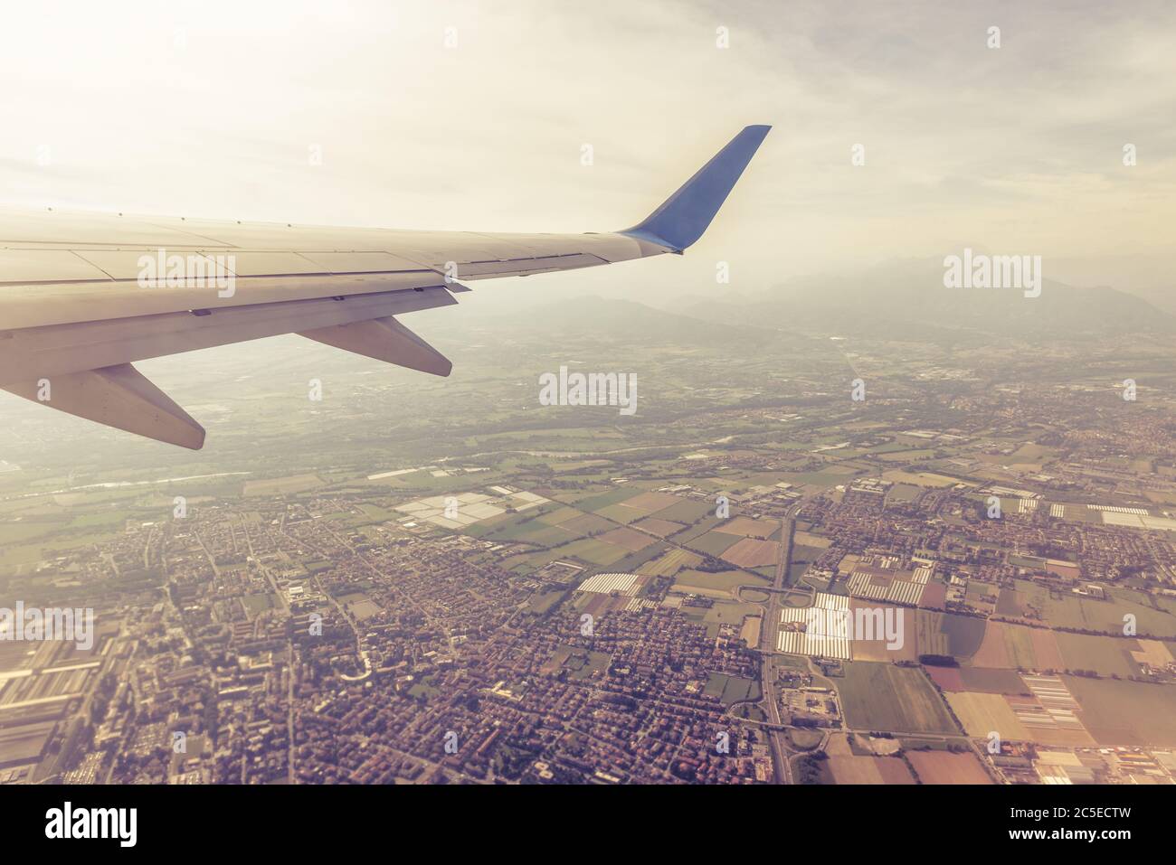 Ala di un aereo che vola sopra città e villaggi. L'ala dell'aereo sullo sfondo del cielo e della terra. Veduta aerea panoramica della terra di motley da airpl Foto Stock