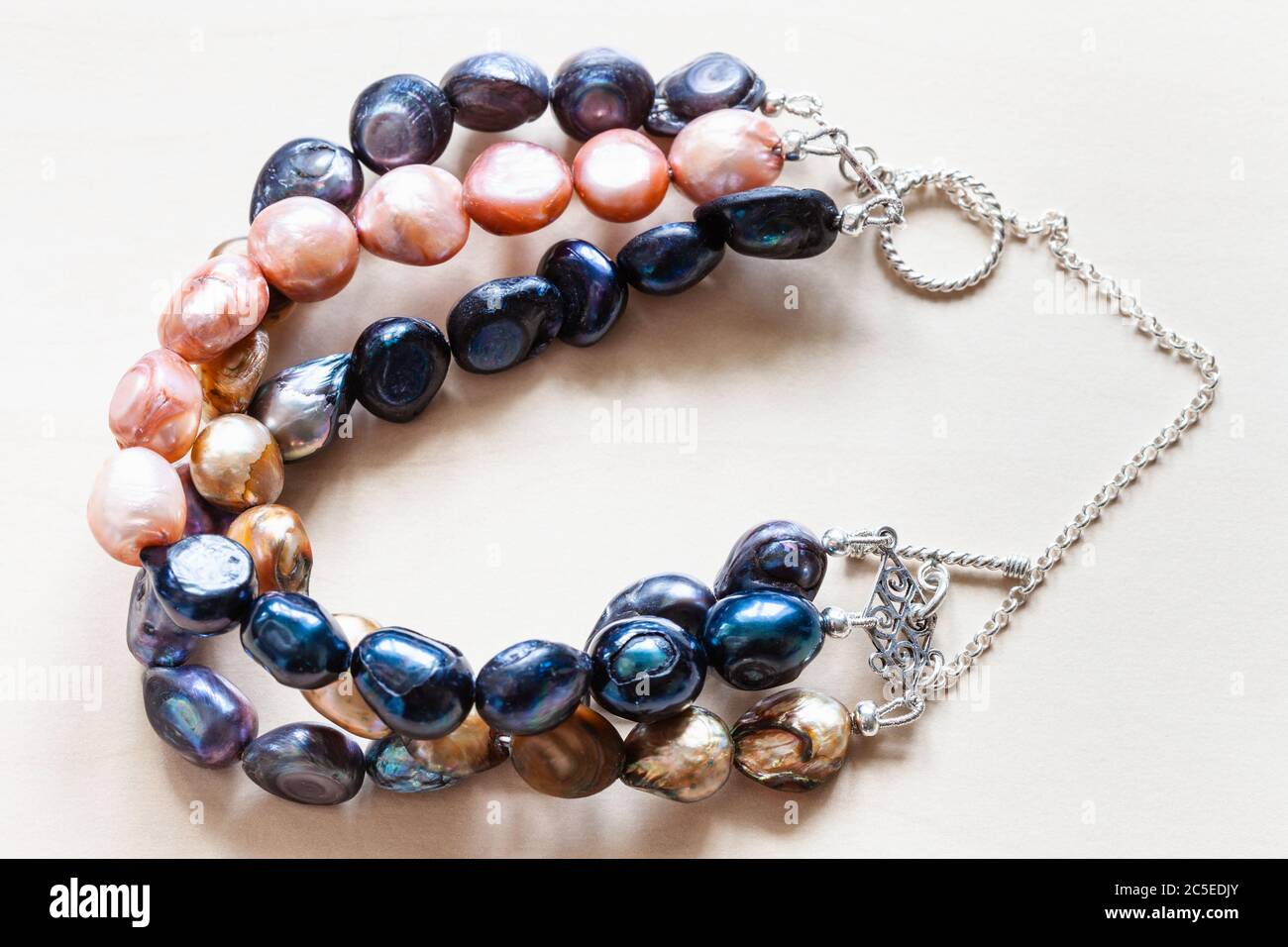 bracciale realizzato a mano da tre palchi di perle di fiume naturali tinte e catena d'argento e closeup a chiusura su tavolo di legno chiaro Foto Stock