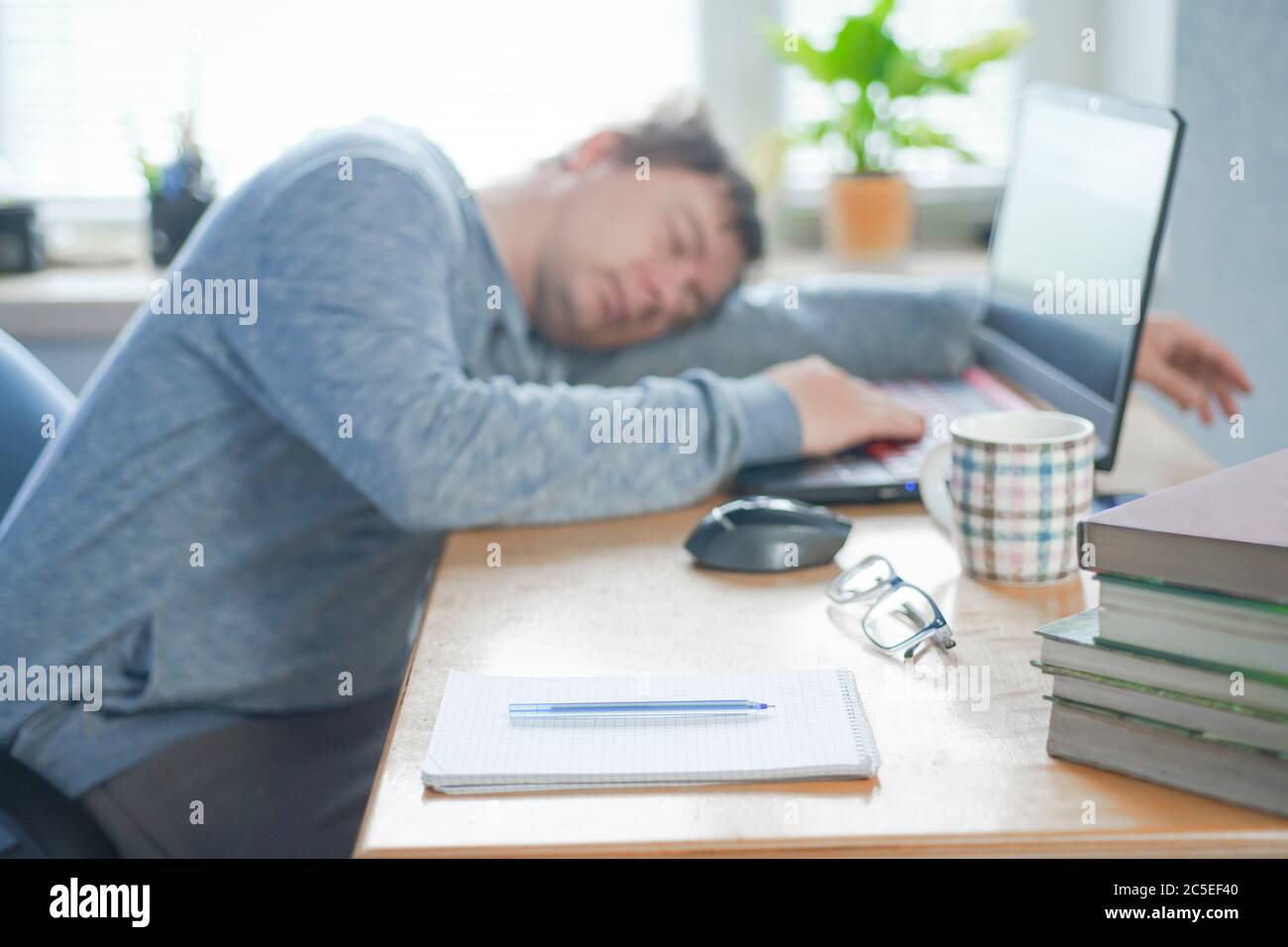 Stanco di un ragazzo studentesco che dormiva sul computer portatile al tavolo Foto Stock