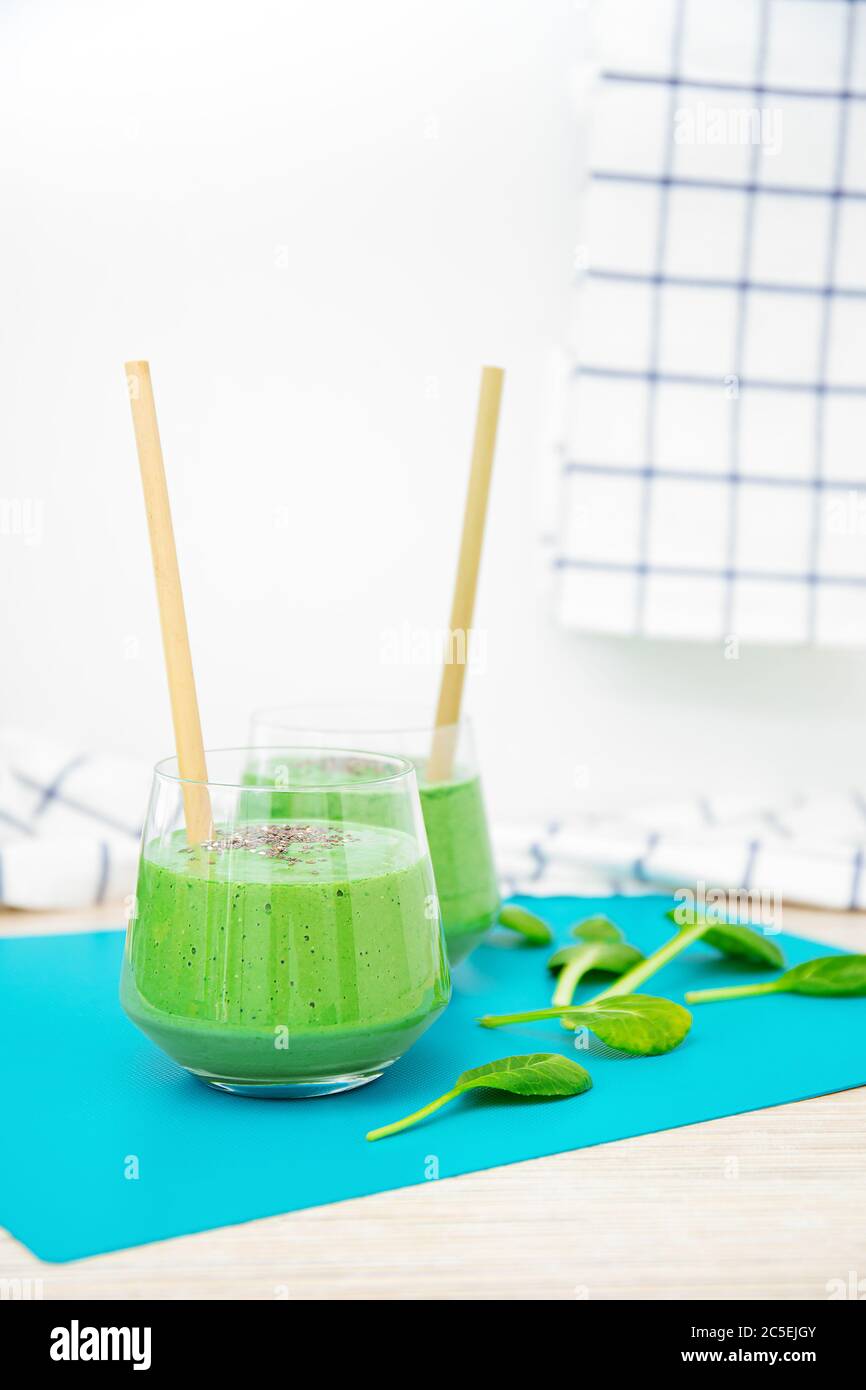 Delizioso frullato di spinaci isolato su sfondo bianco. Eleganti calici in vetro con frullati e tubi di bambù ecologici. Foglie di spinaci. Foto Stock