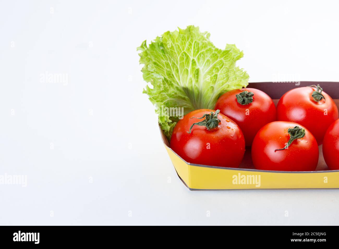 Pomodori rossi succosi in un imballaggio o contenitore ecologico decorato con una foglia di lattuga su uno sfondo bianco isolato. Concetto di eco-friendly Foto Stock