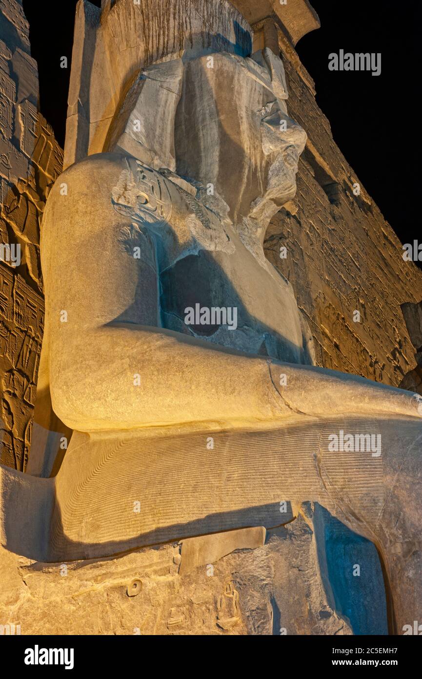 Grande statua di Ramses II all'ingresso del pilone all'antico tempio egiziano di Luxor illuminato durante la notte Foto Stock