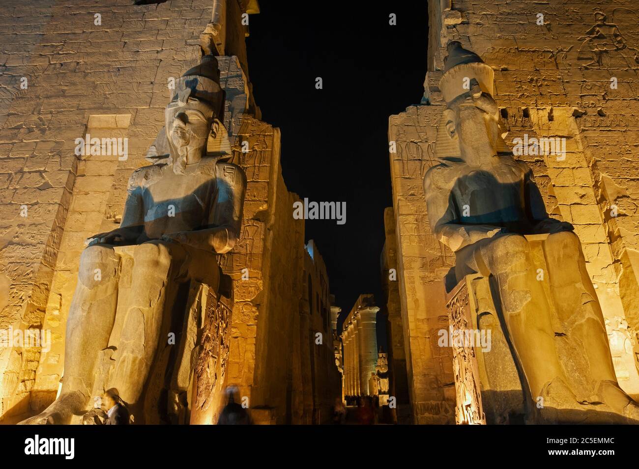 Grandi statue di Ramses II all'ingresso del pilone all'antico tempio egiziano di Luxor illuminato durante la notte Foto Stock