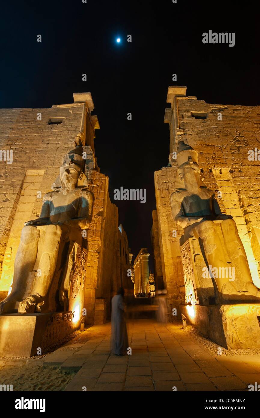 Grandi statue di Ramses II all'ingresso del pilone all'antico tempio egiziano di Luxor illuminato durante la notte Foto Stock