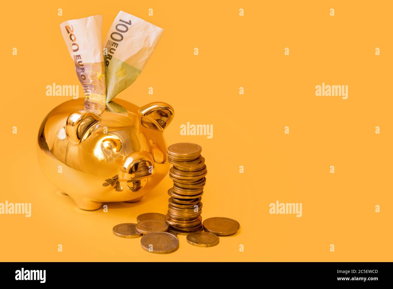 Golden piggy banca con torre di denaro e banconote in euro su sfondo giallo. Pila di monete in euro vicino al contenitore di denaro dorato. Denaro maiale, risparmio di denaro, Moneybox Foto Stock