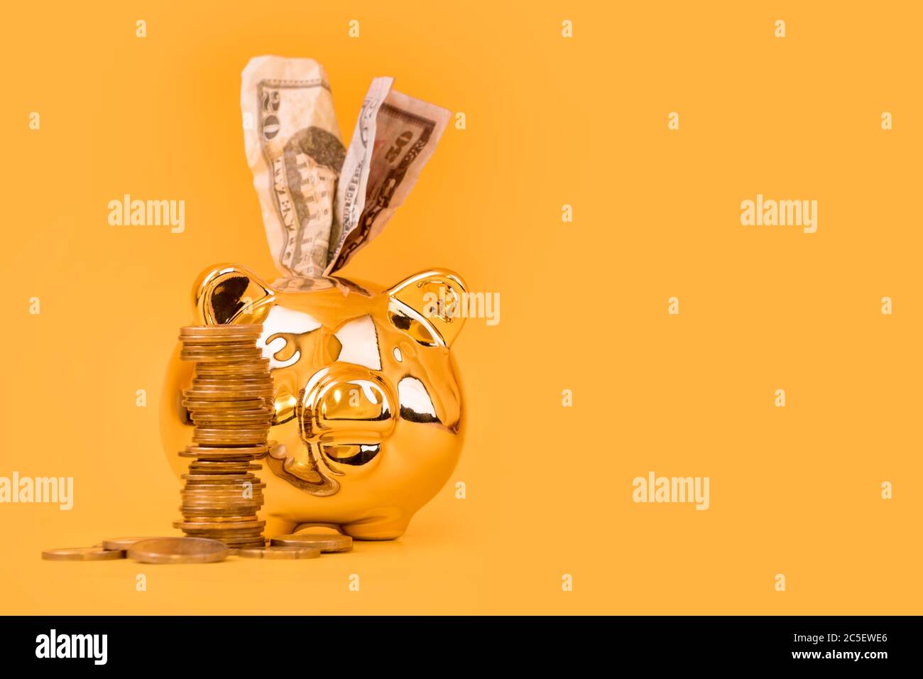 Golden piggy banca con torre di denaro e dollari bollette su sfondo giallo. Pila di monete in euro vicino al contenitore di denaro dorato. Denaro maiale, risparmio di denaro, Moneybox Foto Stock