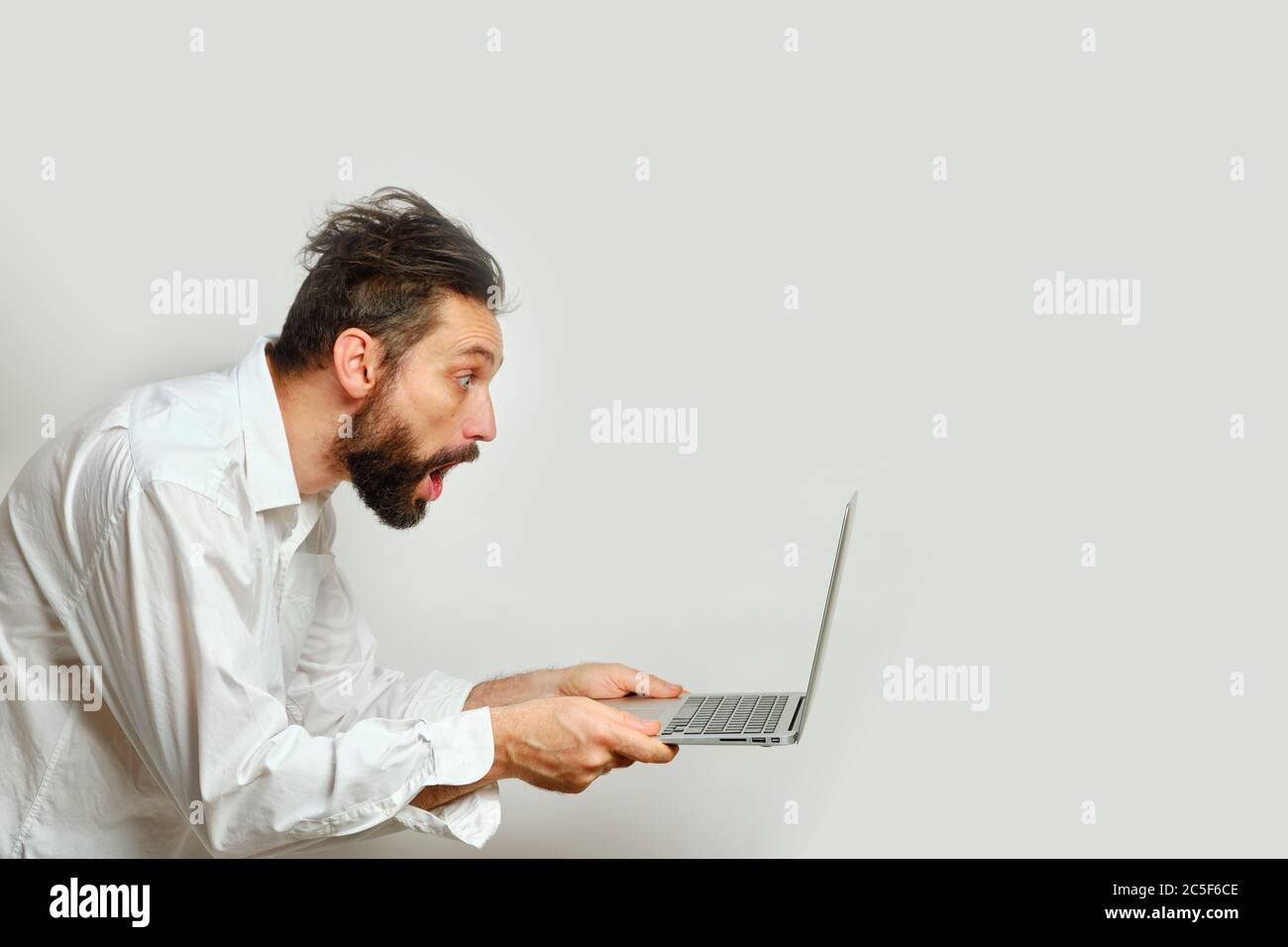 Un giovane caucasico guarda a sorpresa un monitor per computer portatile isolato su sfondo bianco. Emozioni umane, concetto di espressione facciale Foto Stock