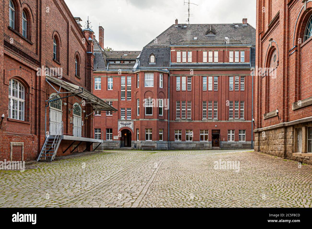 Un cortile lastricato a ciottoli della birreria Landskron a Görlitz, Sassonia, è incorniciato da edifici in mattoni a più piani con finestre a bovindo, piccole torrette e una scala esterna. La birreria, fondata nel 1869, ha fatto erigere la maggior parte dei suoi edifici in mattoni tra il 1907 e il 1916. Foto Stock