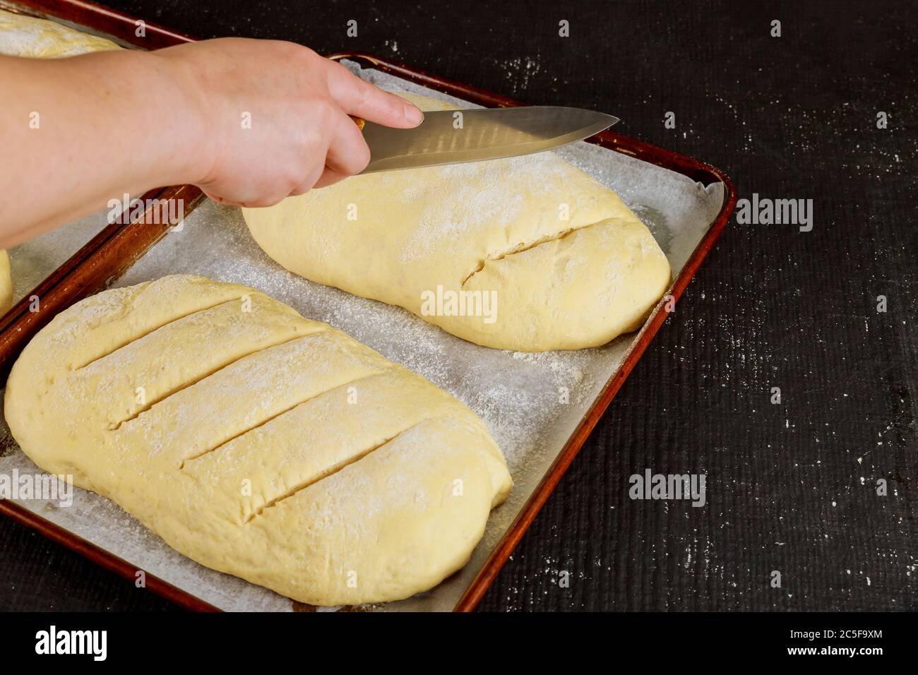 La donna taglia su rack l'impasto di pane fatto in casa non cotti pronto per la cottura. Foto Stock