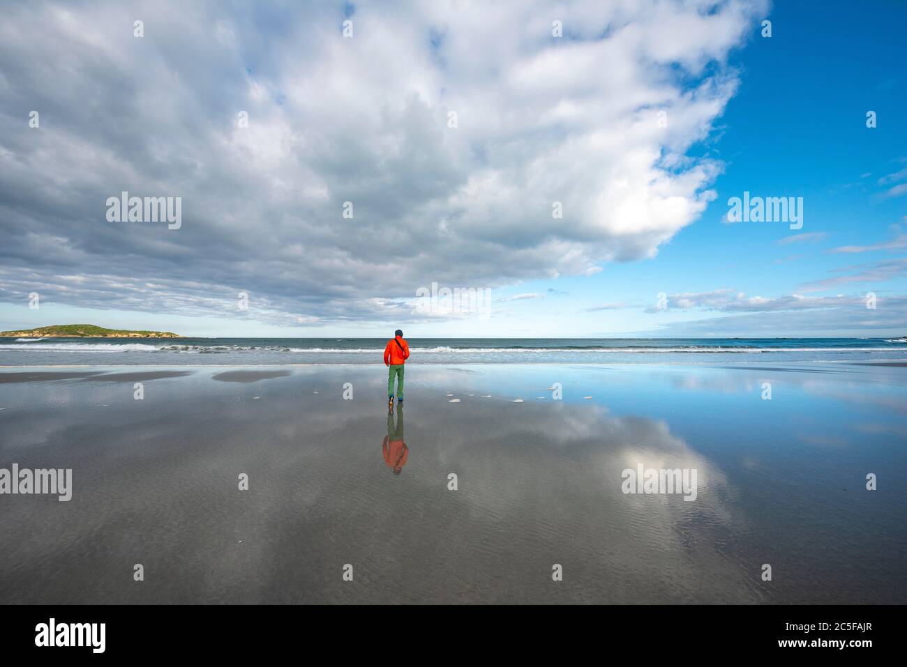 Riflessione, giovane uomo che cammina sulla grande spiaggia sabbiosa a bassa marea, Taieri Beach, Isola del Sud, Nuova Zelanda Foto Stock
