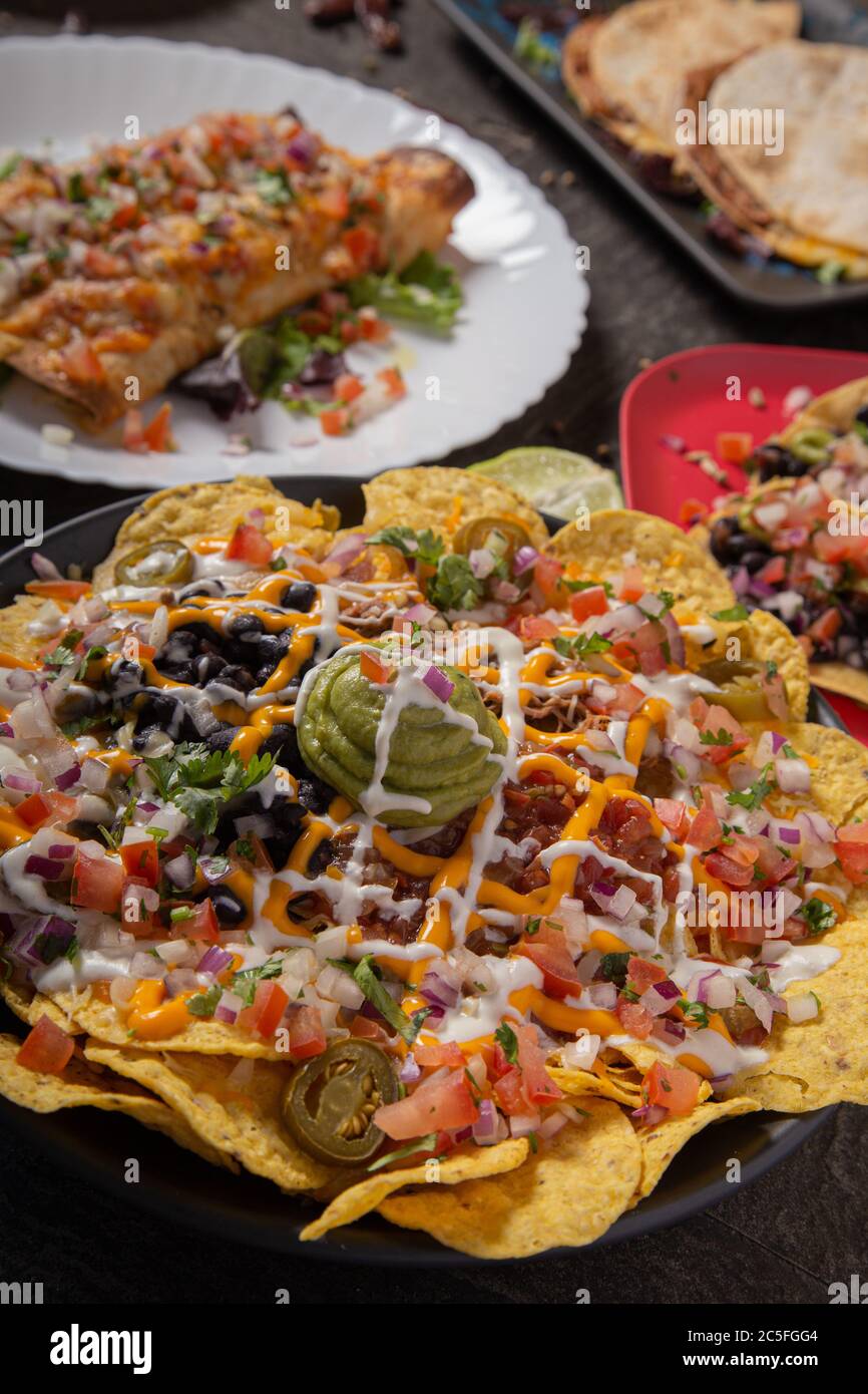 Un piatto di deliziosa tortilla nachos con salsa al formaggio fuso, carne tritata, peperoni jalapeno, cipolla rossa, cipolle verdi, pomodoro, olive nere, salsa e. Foto Stock