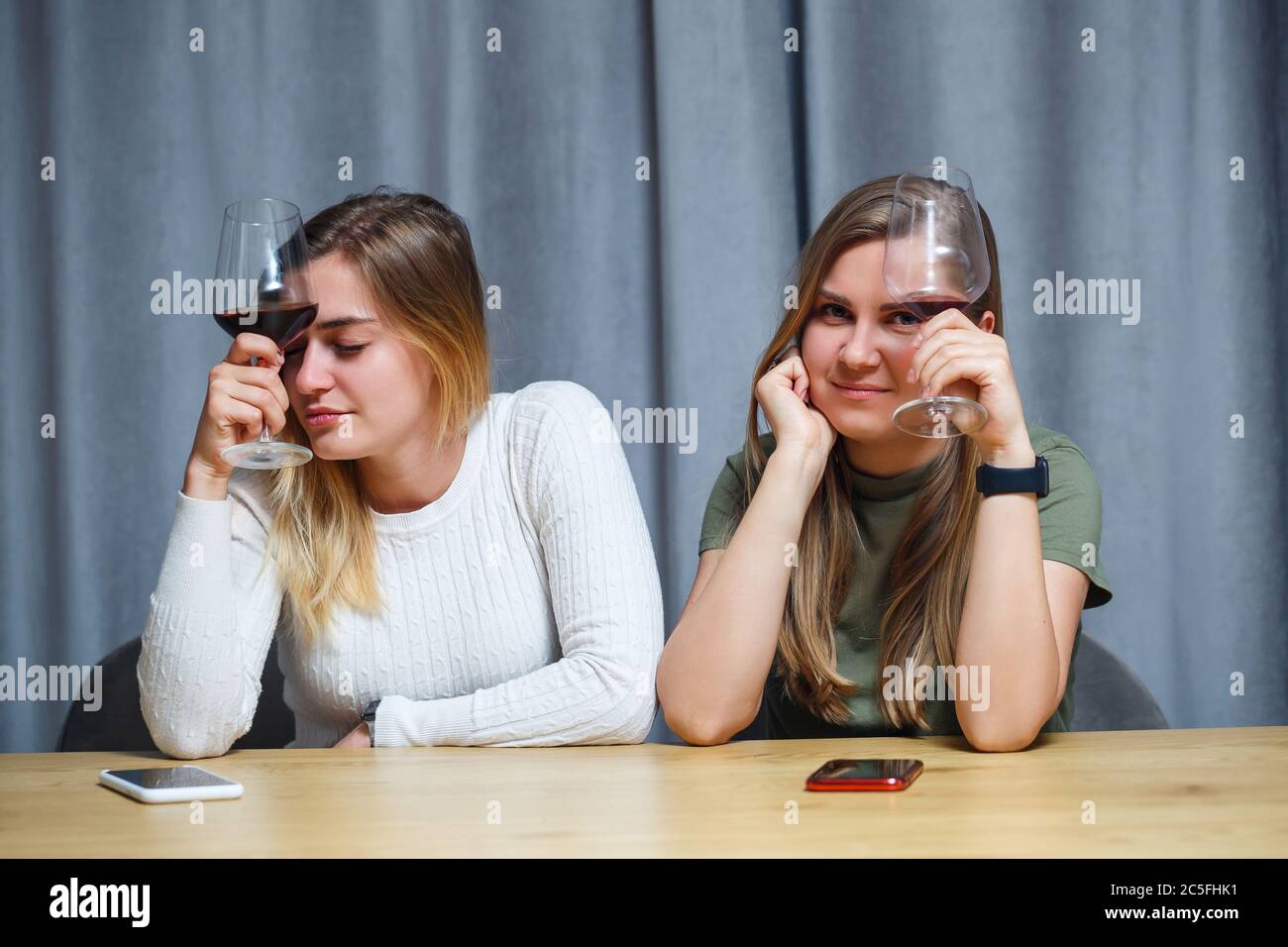 Due ragazze di aspetto europeo sono sedute al tavolo con bicchieri di vino. Conversazione di fidanzate con bevande alcoliche. Foto Stock