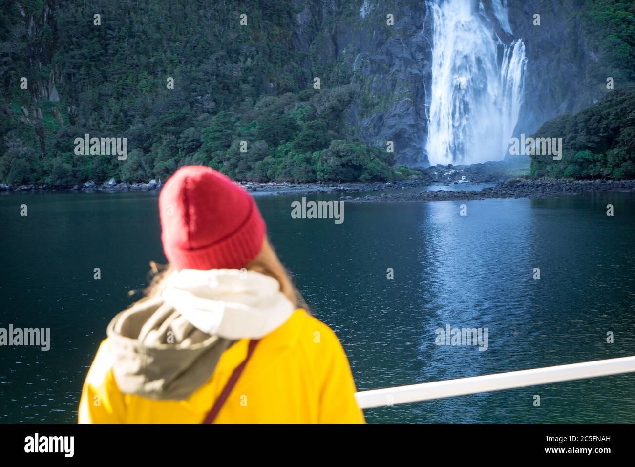 Una donna turistica su una barca da crociera che guarda una bella cascata a Milford Sound, Nuova Zelanda Foto Stock