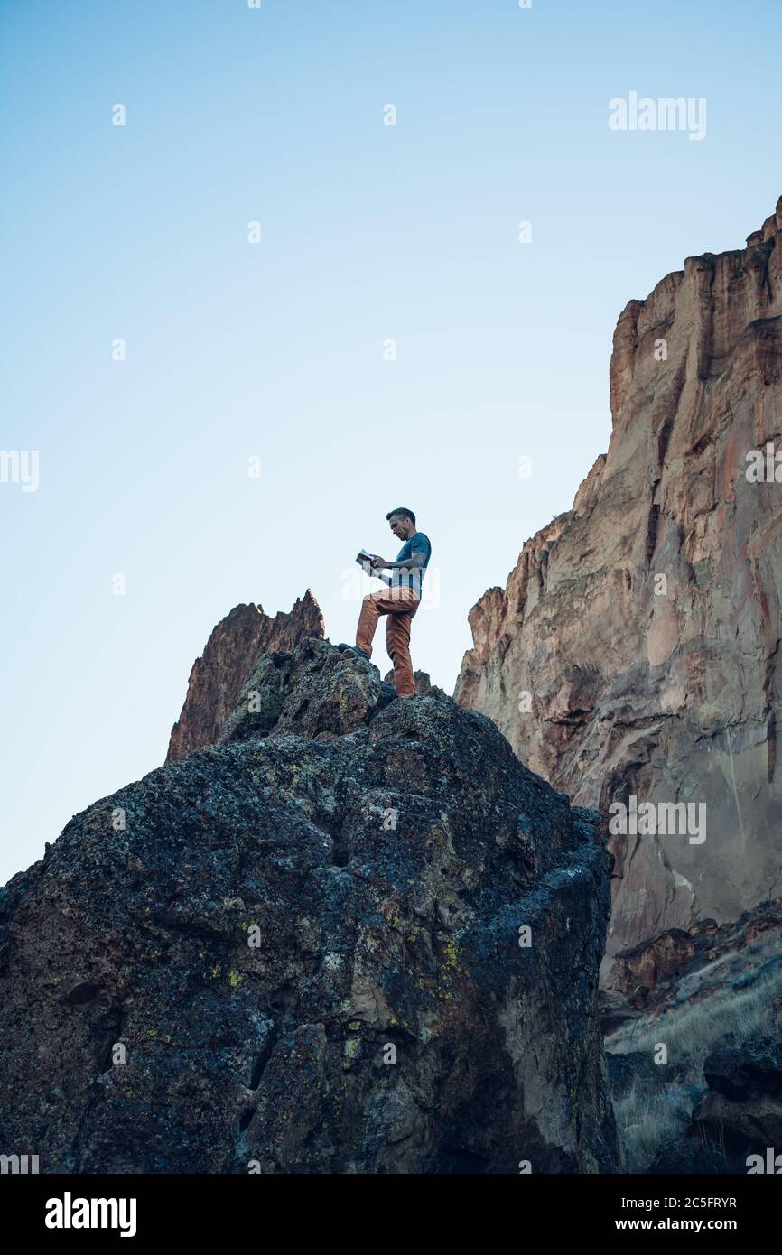 Alpinista maschile che legge un libro di guida sulla parte superiore di Il masso in Oregon Foto Stock