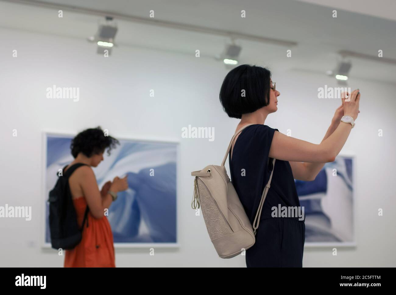 Mosca 11/06/2019 Donna scatta foto in mostra fotografica con smartphone, altra ragazza che usa messaggero o social network sul suo cellulare, invece Foto Stock