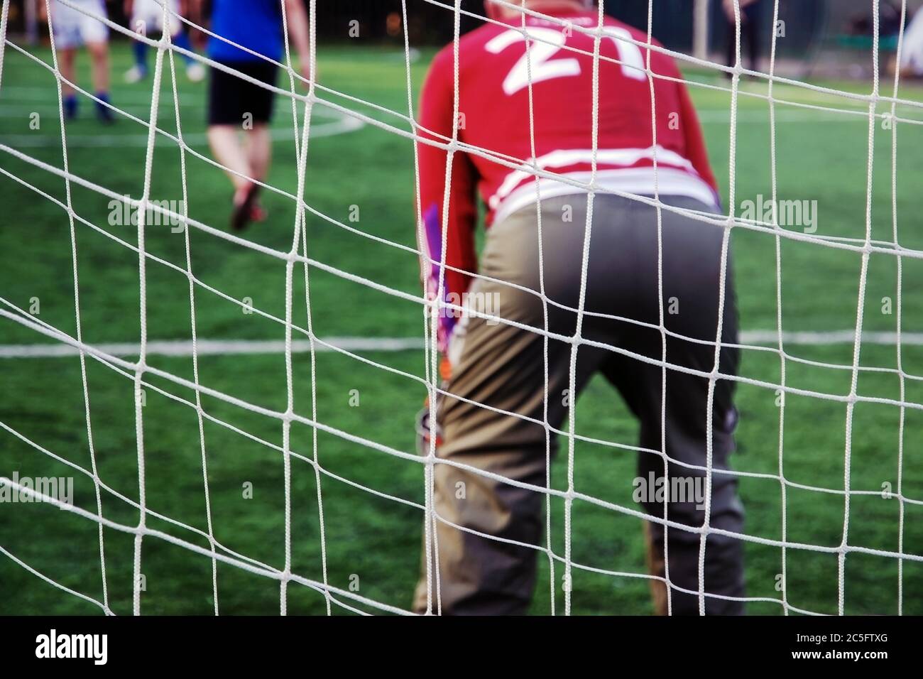 Squadra di calciatori dilettanti con portiere senior in uniforme rossa sotto il numero 21 giocando a calcio nel parco giochi gratuito nel parco pubblico. Schiena di anziani Foto Stock