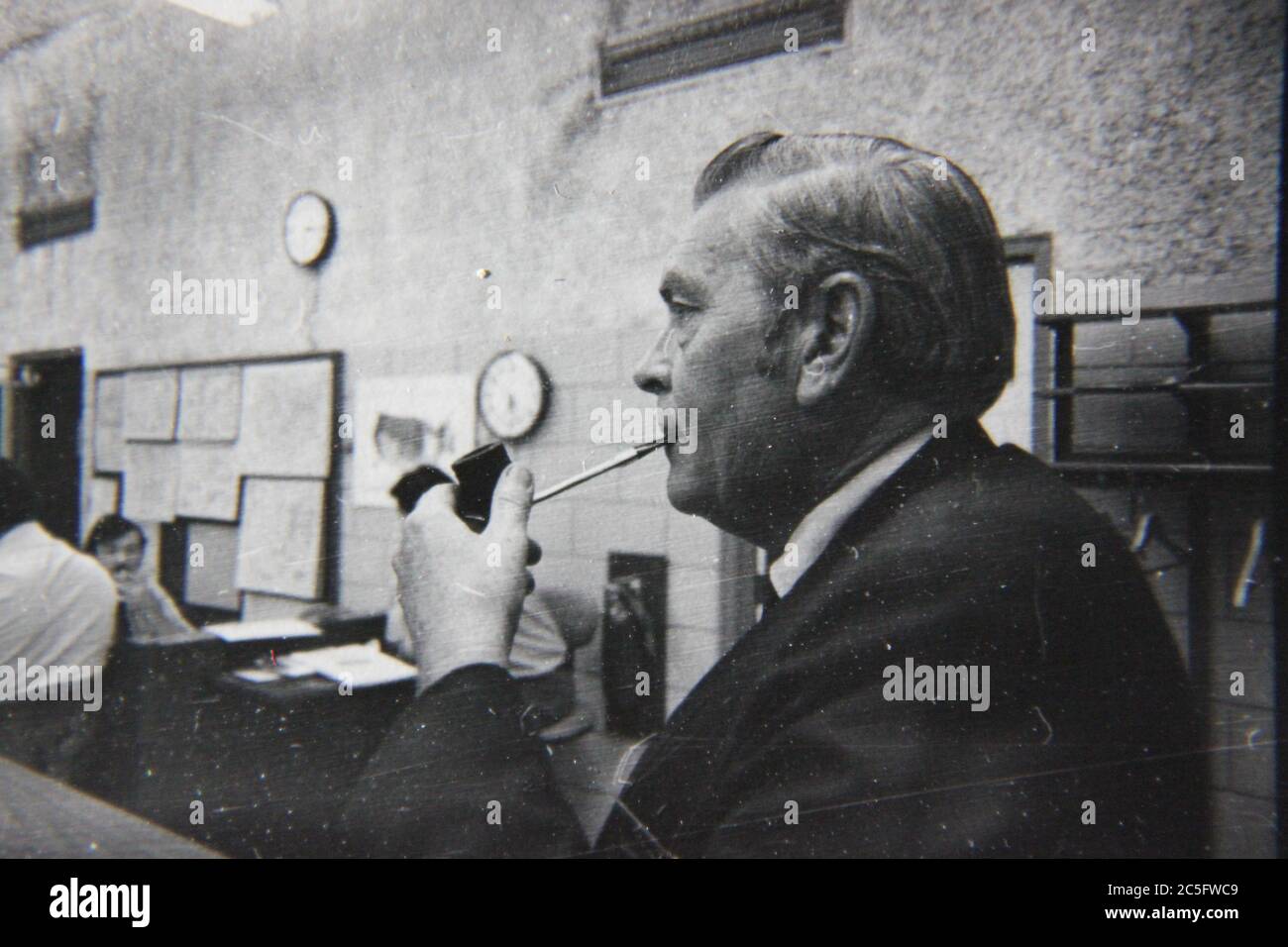 Fine anni '70 vintage nero e bianco stile di vita fotografia di un dipendente regolare fumare un sigaro in ambiente di ufficio. Foto Stock