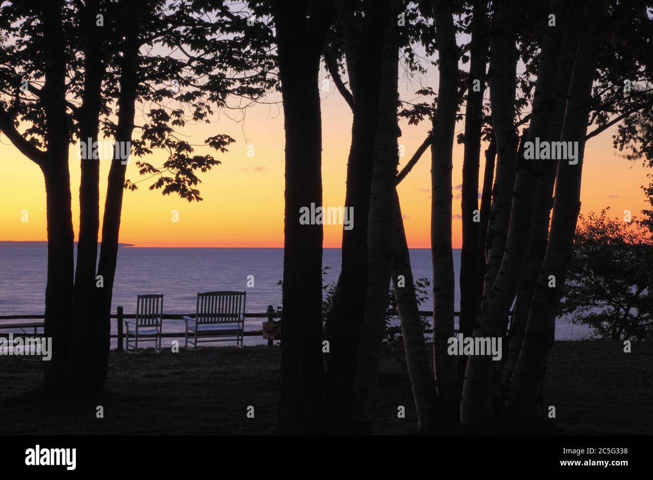 Chippewa County MI / Oct UN paio di sedie sul lago Whitefish Bay Superior sono incorniciati all'alba da tronchi silhouette di Scarlet Maple. Foto Stock