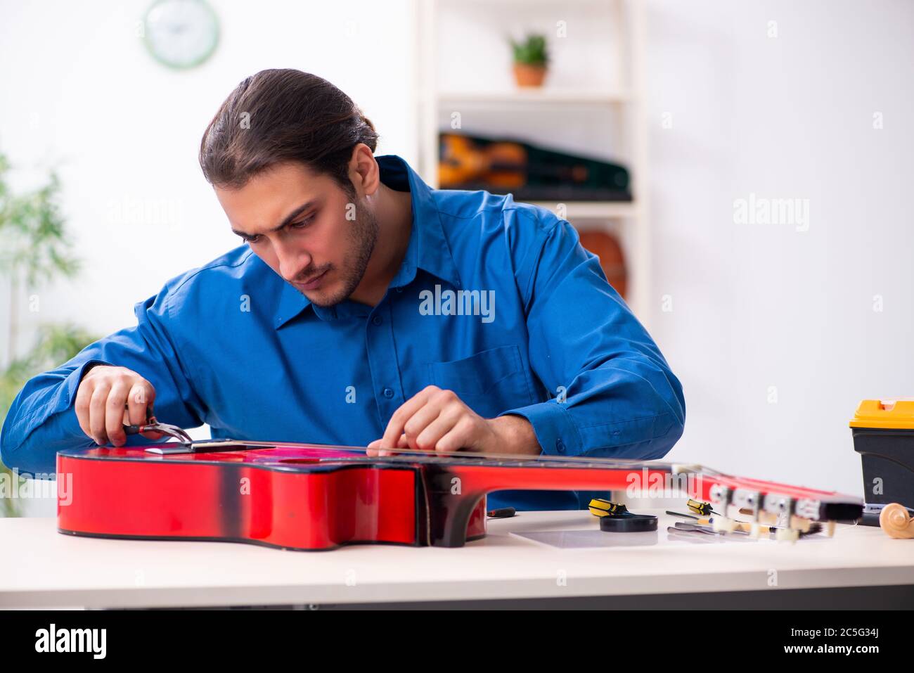 Giovane uomo riparatore riparando la chitarra Foto Stock