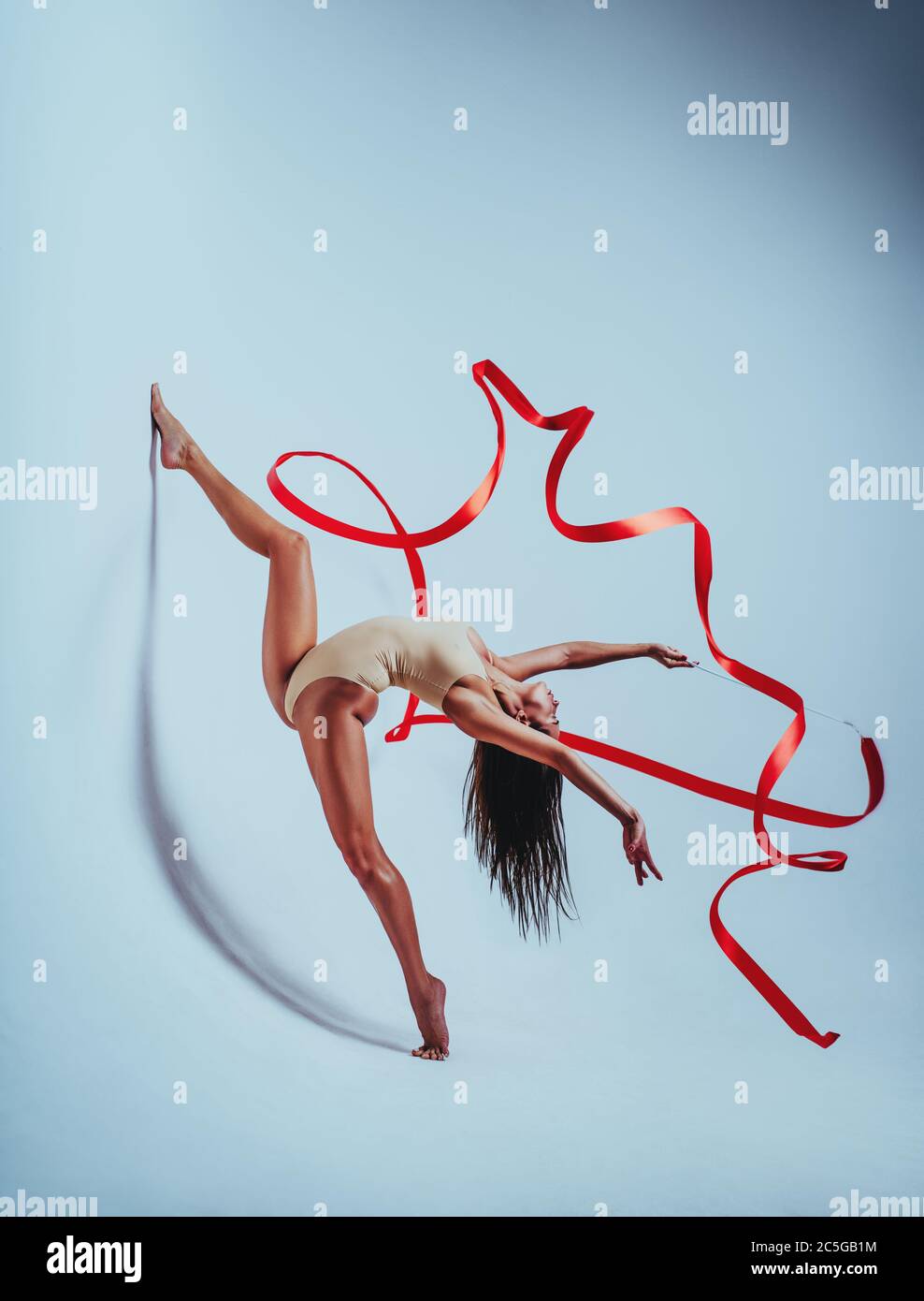 Giovane donna ginnastica che balla con nastro rosso su sfondo bianco Foto Stock