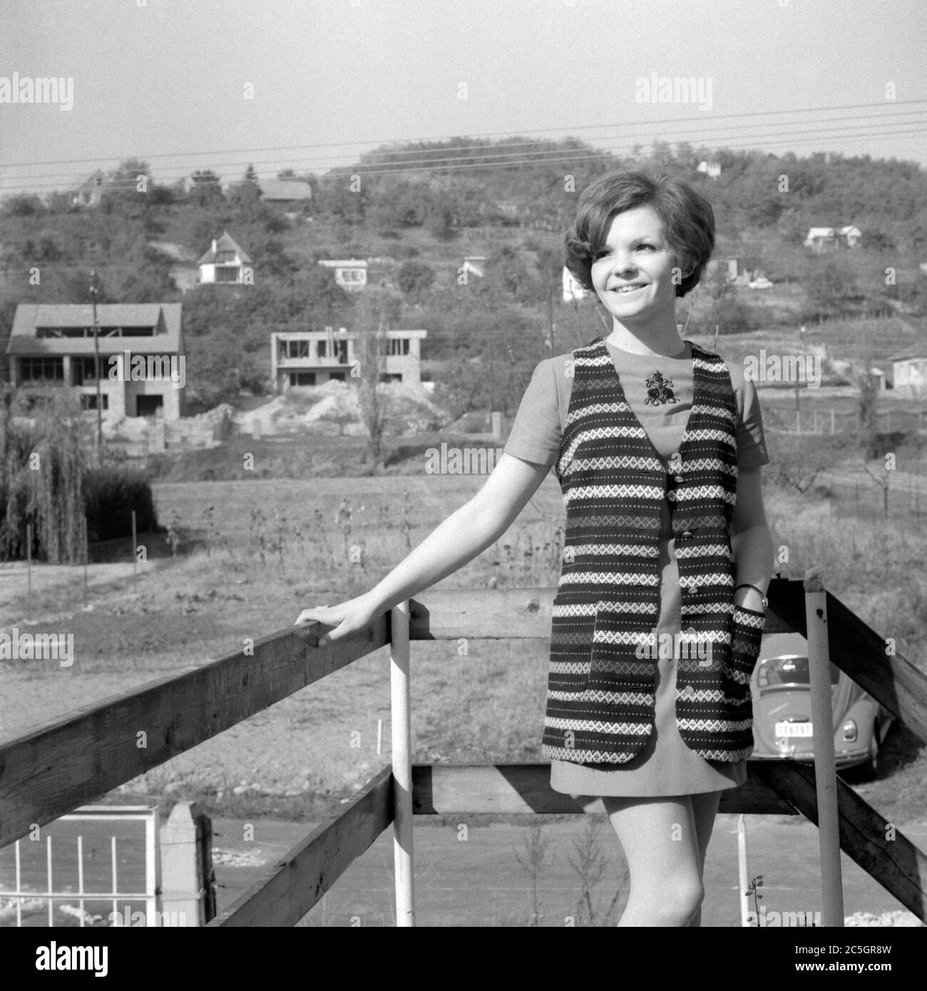 sorridente giovane donna che indossa mini abito in piedi tra le nuove case di costruzione sul sito degli anni '60 ungheria Foto Stock