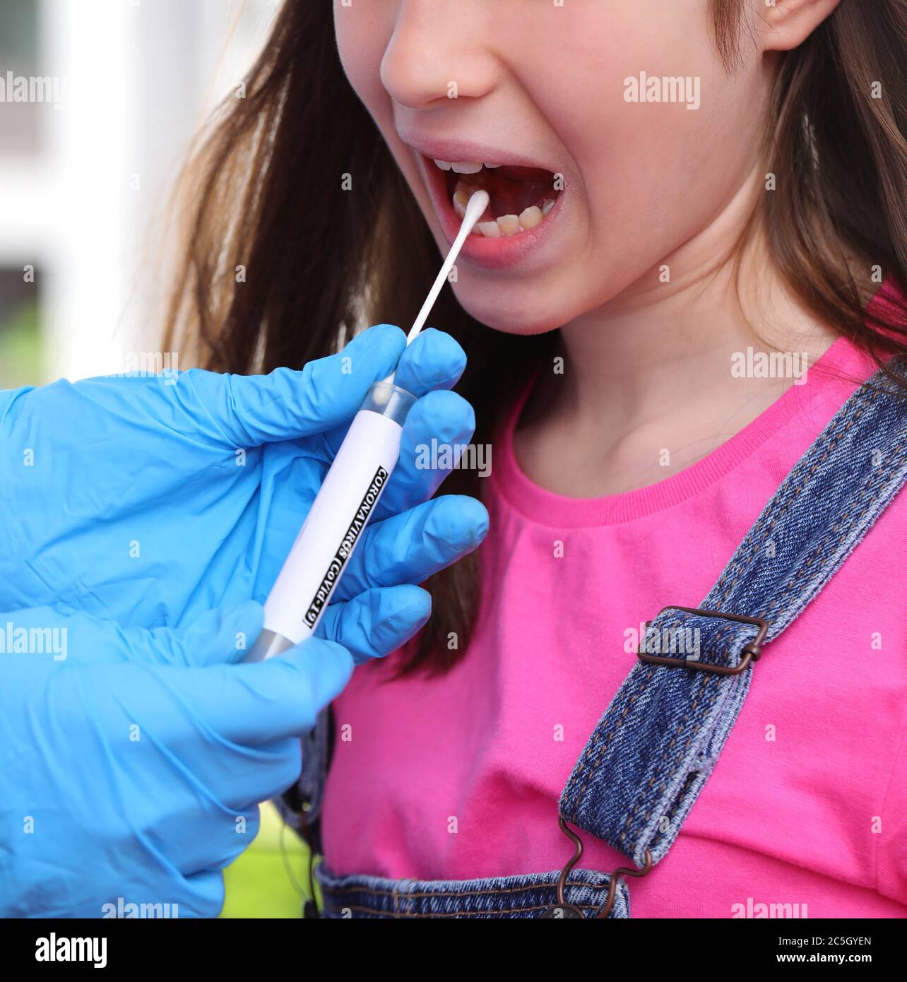 medico con guanti in lattice fa un bastoncino alla ragazza con la bocca aperta per cercare il coronavirus Foto Stock