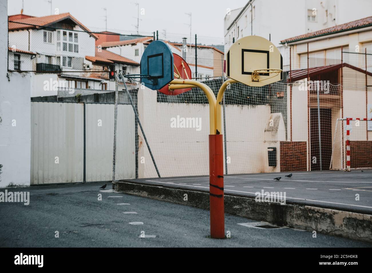 Campo da gioco vuoto scuola asfalto nel cortile con tre cestini colorati per il basket e parte per pallamano in background Foto Stock Campo da gioco vuoto scuola asfalto nel cortile con tre cestini colorati per il basket e parte per pallamano in background Foto Stock