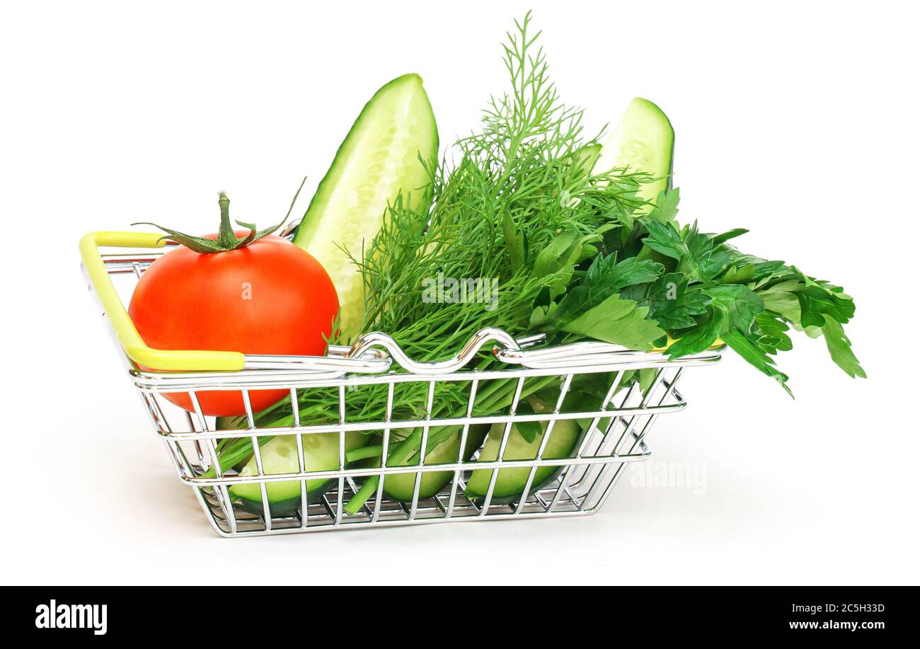 un piccolo cestino con erbe, cetriolo, pomodoro, prezzemolo accanto ad un'insalata verde in vaso su sfondo bianco. Cibo sano, cibo vegetariano, Foto Stock