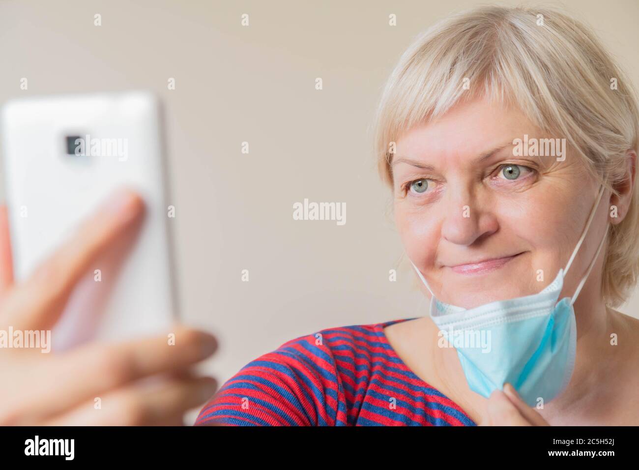 Donna matura che prende selfie tenendo in mano la maschera medica. Donna anziana che prende la maschera medica faccia facendo selfie. Selfie di donna anziana senza maschera Foto Stock