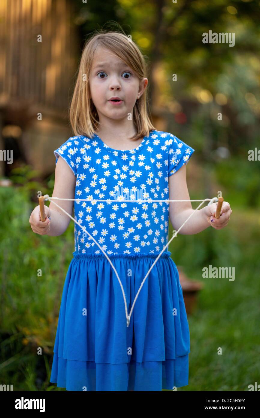 Giovane ragazza in un vestito blu e bianco che soffia grandi bolle con corda in un cortile posteriore Foto Stock