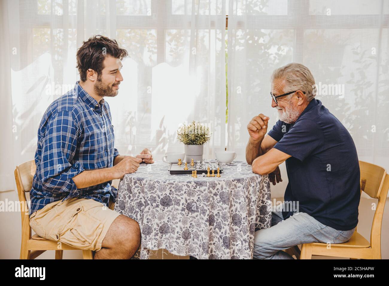 Anziano intelligente giocare gioco di scacchi a casa cura con l'uomo più giovane per rimanere in salute cervello Foto Stock