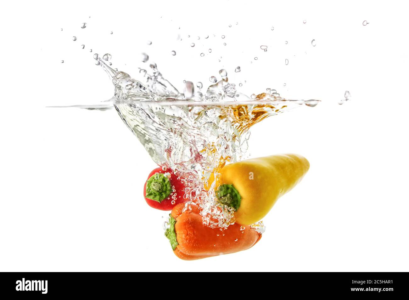 Peperoni rossi e arancioni cadono in acqua con spruzzi e bolle, Foto Stock
