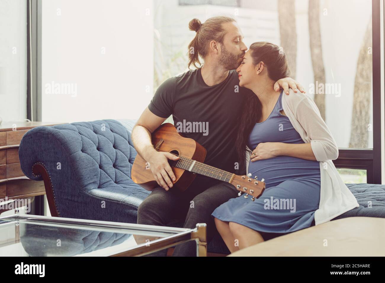 Marito con la moglie incinta stare a casa bella suonare la musica della chitarra per il bambino baciare e mostrare l'amore insieme Foto Stock