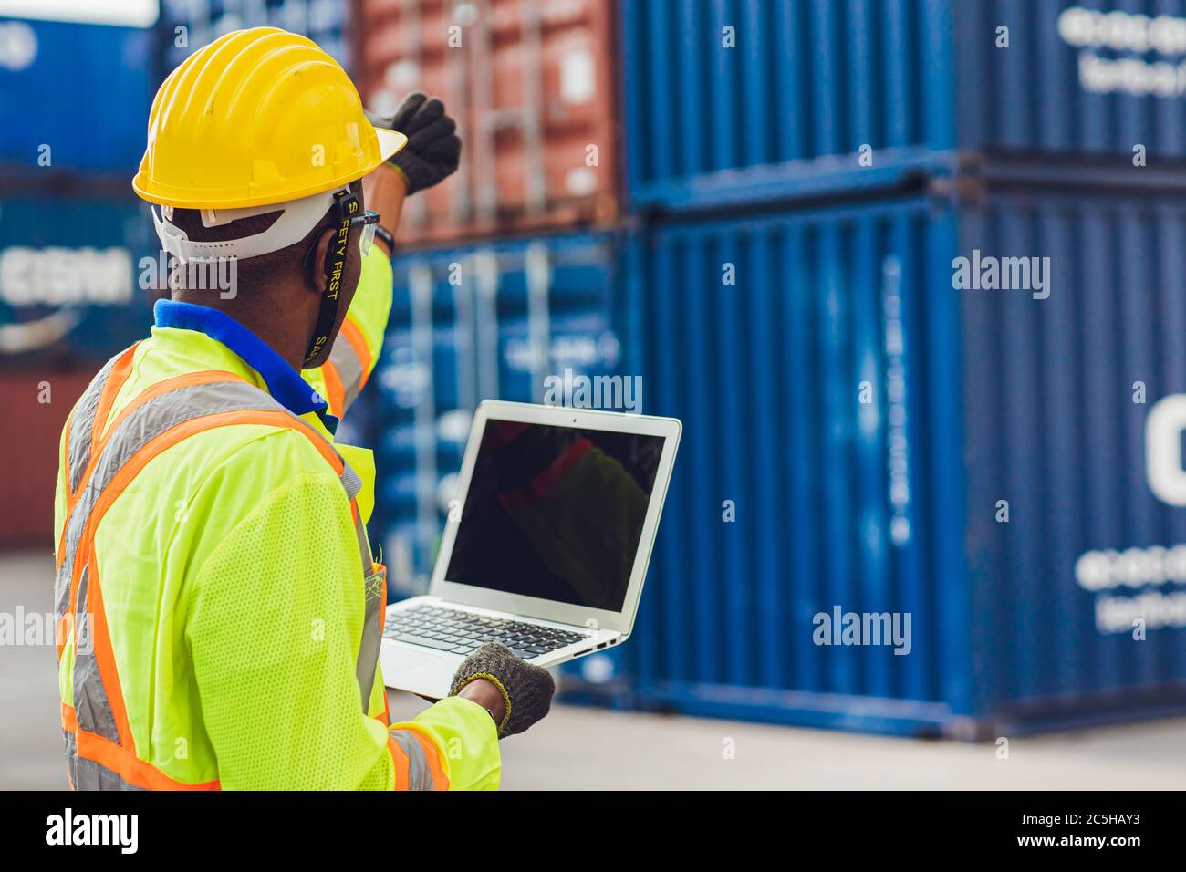 Computer portatile schermo vuoto con vista posteriore del personale di caposquadra che lavora in controllo logistico caricare i contenitori al porto carico a camion per l'esportazione Foto Stock