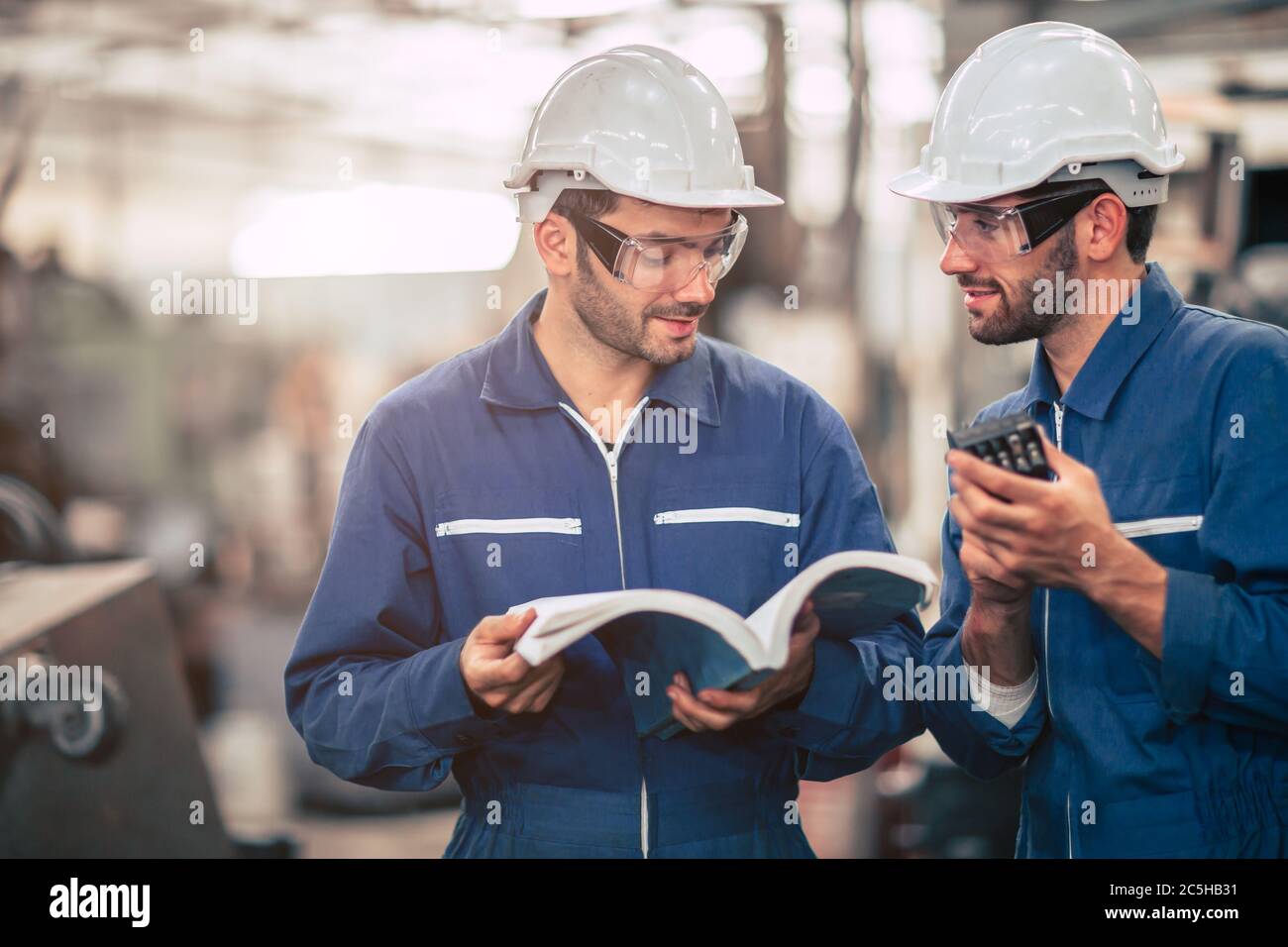 Il team di ingegneri che parla insieme insegna e impara a conoscere l'uso della macchina con un manuale di istruzioni aperto sul luogo di lavoro della fabbrica. Foto Stock
